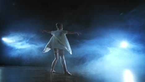 Modern-dance-woman-in-a-white-dress-dances-a-modern-ballet-jumps-on-the-stage-with-smoke-in-the-blue-spotlights.